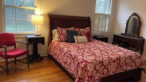 Une chambre à coucher avec un lit en bois, une chaise, une table de chevet, une commode et une lampe.
