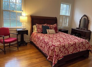 A bedroom with a wooden bed, a chair, a nightstand, a dresser, and a lamp. - Walk to MSU, Downtown & Cotton District  Historic Home, Sleeps 6 (Starkville)