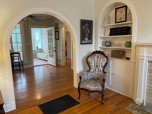 Una habitación con piso de madera, un sillón estampado, una chimenea y una estantería.