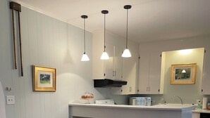 Una cucina moderna con mobili bianchi, un'isola centrale, luci a sospensione e due poltrone imbottite.