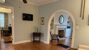 Un salon spacieux doté d’un plancher en bois franc, d’un téléviseur fixé au mur, d’une cheminée et d’un coin salon confortable.