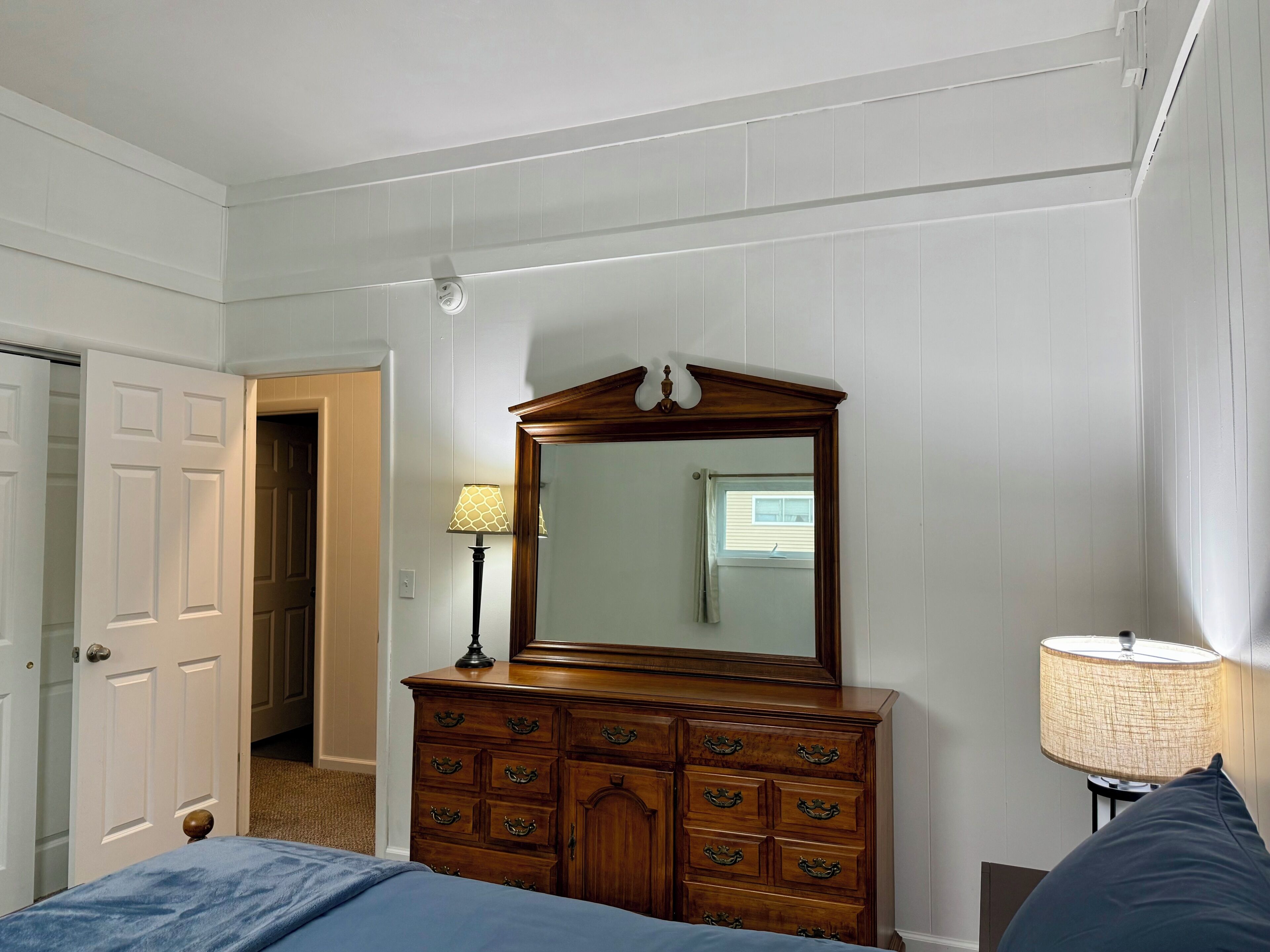 A bedroom with a wooden dresser, a mirror, a lamp, and a bed.