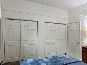 A bedroom with two white doors, a bed with a blue blanket, and a wooden dresser. - 2-bedroom apartment in quiet neighborhood in Watertown. (Watertown)