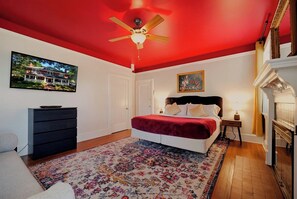 Ein Schlafzimmer mit einem Bett, Deckenventilator, Kamin, einem Gemälde und einer Kommode.