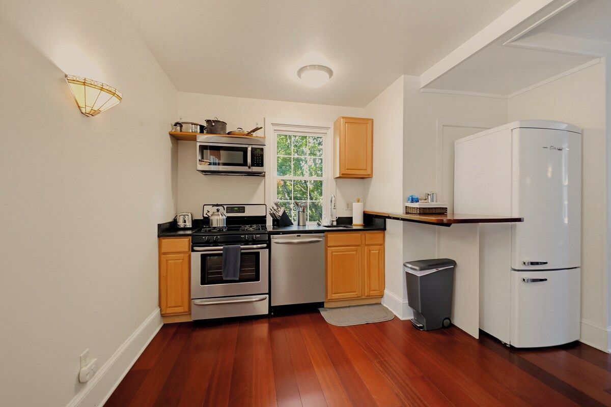 A compact kitchen with wooden cabinets, a microwave, a stove, a dishwasher, and a white refrigerator.