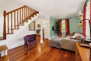 Una sala de estar con una escalera de madera, un sillón morado, un sofá y una mesa de comedor.