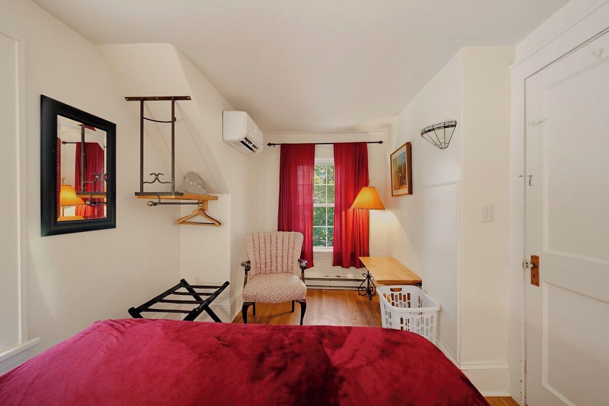 Une chambre à coucher avec un lit, une chaise, un bureau, une fenêtre avec des rideaux et une porte.