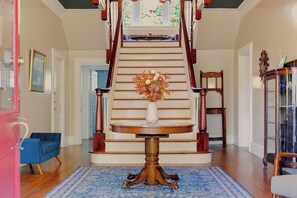 A grand staircase with a vase of flowers on a table at the bottom. - Sweet Biscuit Inn | 2 Homes • Sleeps 26 (Asheville)