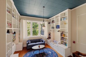 A room with a blue ceiling, white built-in bookshelves, a grey sofa, a small round table, and a patterned rug. - Sweet Biscuit Inn | 2 Homes • Sleeps 26 (Asheville)