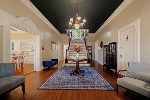 A spacious foyer with a grand staircase, a chandelier, and a dining area with a table and chairs. - Sweet Biscuit Inn | 2 Homes • Sleeps 26 (Asheville)