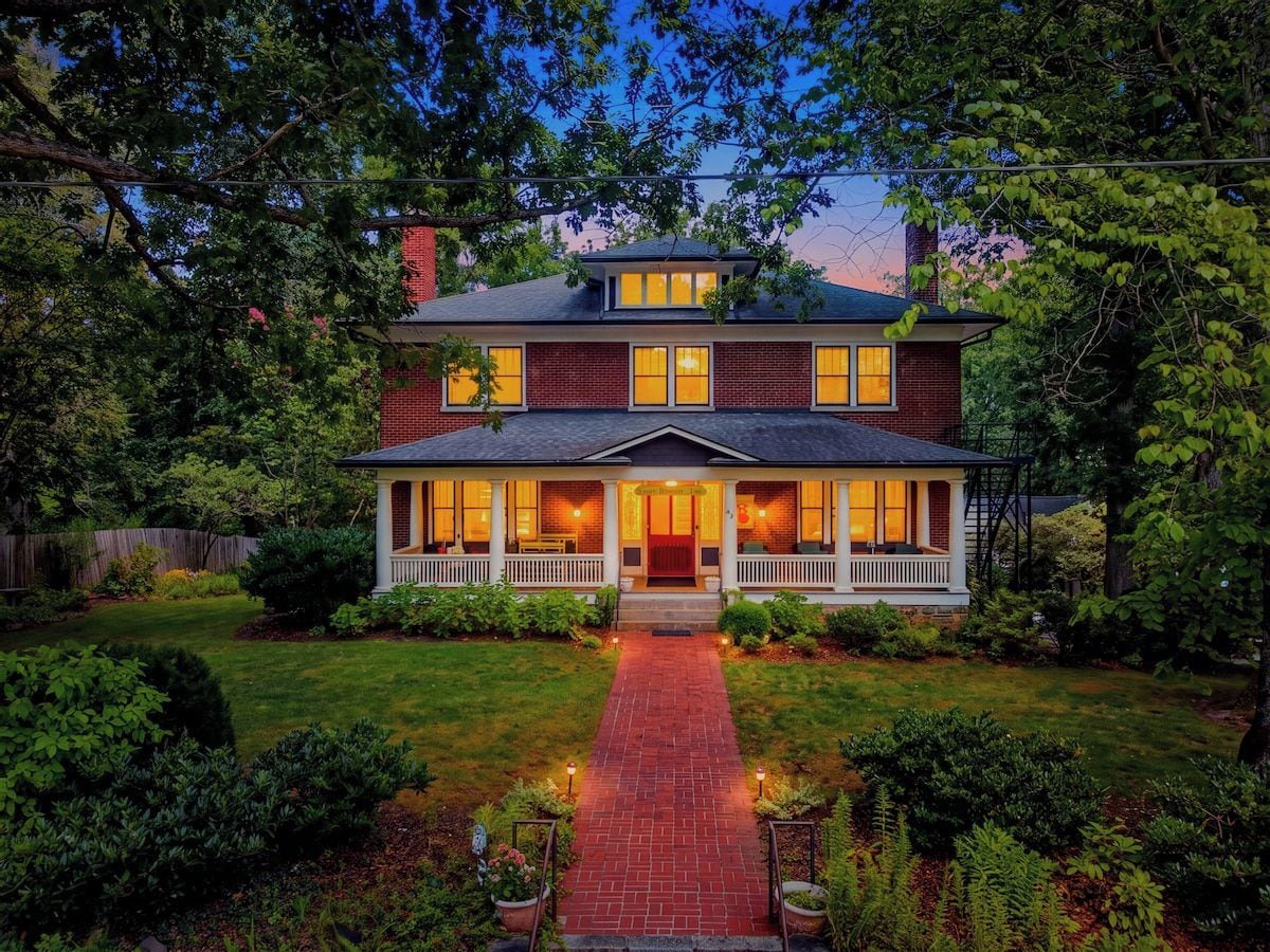 A two-story house with a front porch, a brick facade, and a pathway leading to the entrance.