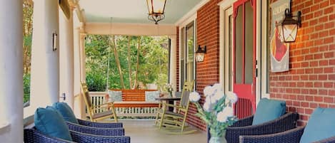 A covered porch with wicker furniture, a glass table, and a brick wall.