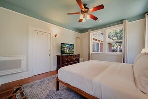 A bedroom with a bed, a ceiling fan, a television, and a window with curtains. - Sweet Biscuit Inn | 2 Homes • Sleeps 26 (Asheville)