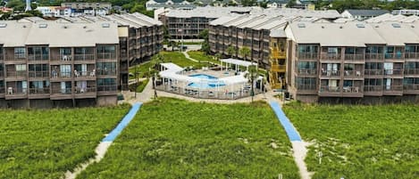 A multi-story hotel with a central courtyard, outdoor pool, and beach access.