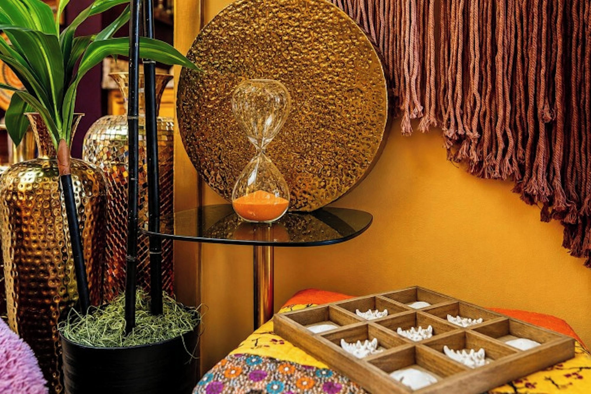 A room with a round mirror, a potted plant, a table with a colorful tablecloth, and a wooden box with compartments.