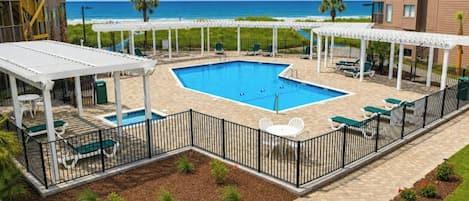Un espace piscine avec vue sur la plage, entouré de chaises longues et doté d’un coin salon abrité.