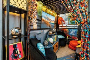 Una habitación con un sofá azul, un sillón negro, un armario de madera y una cortina de cuentas coloridas.