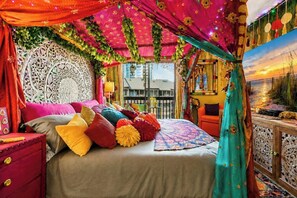 Una habitación con una cama, una mesita de noche roja, un cortinón verde azulado y un detalle decorativo en la pared.