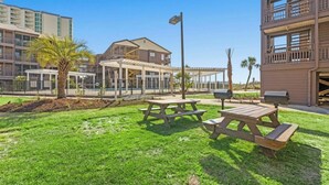 Un'area verde all'aperto con tavoli da picnic e barbecue, circondata da edifici con balconi e porticati.
