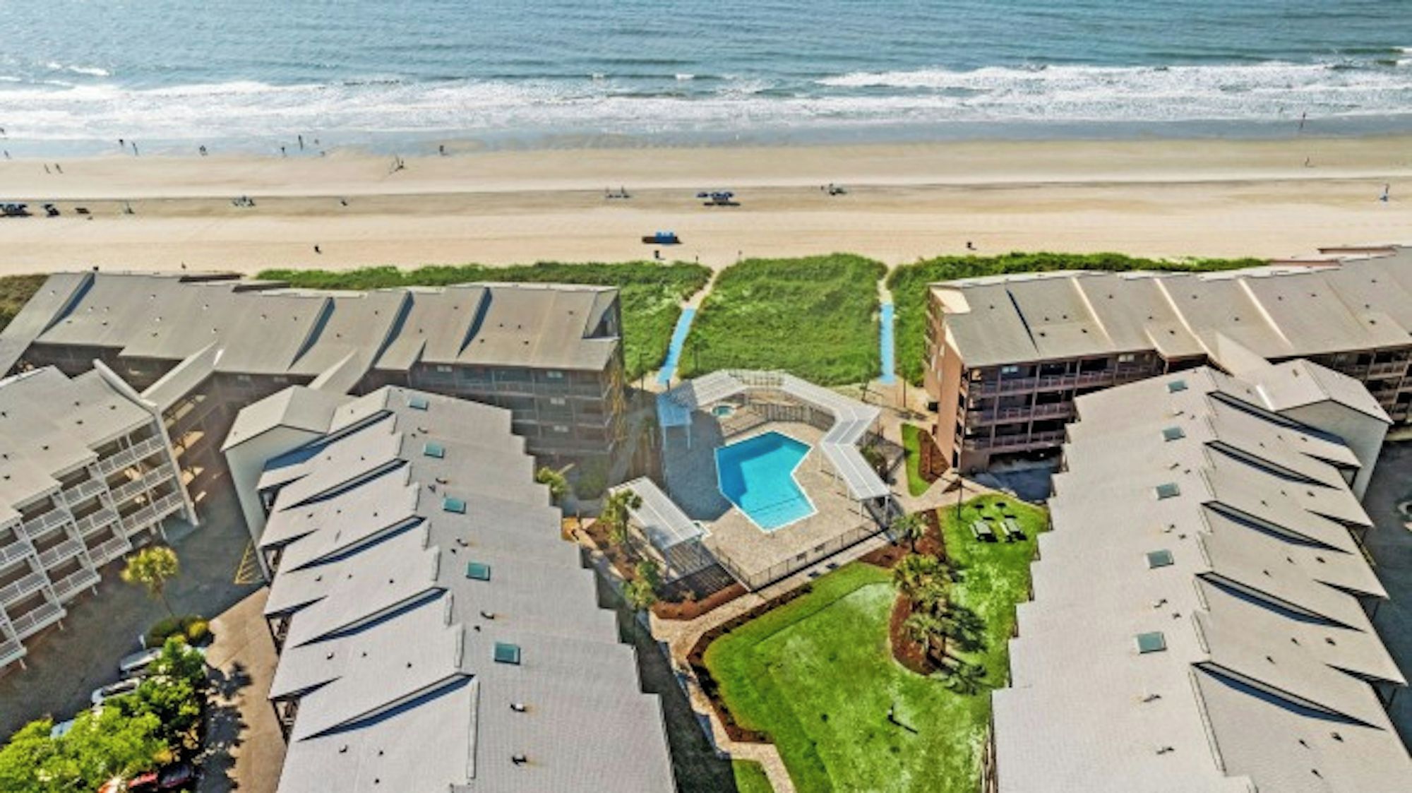 Ein Resort mit mehreren Gebäuden, einem zentralen Pool und Blick auf den Strand.