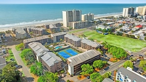 Un hotel costero con varias edificaciones, una cancha de tenis y vista al mar.