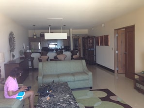 A living room with a sofa, a coffee table, and a person using a laptop. There is a kitchen in the background. - 3-bedroom Ocean Front Villa, Dawn Beach Club at JW Marriott. Fixed 6403 (oyster pond)