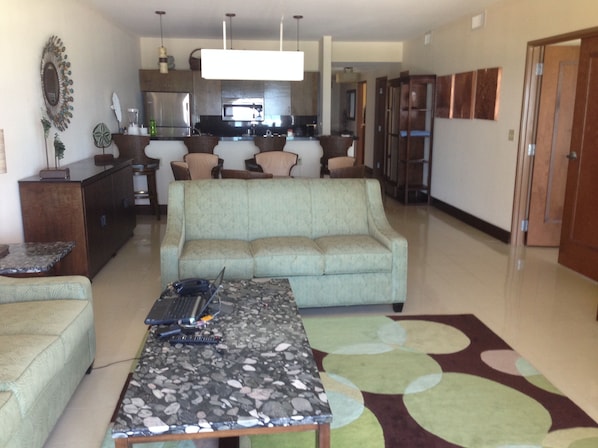 A living room with a sofa, a coffee table, and a kitchen in the background. - 3-bedroom Ocean Front Villa, Dawn Beach Club at JW Marriott. Fixed 6403 (oyster pond)