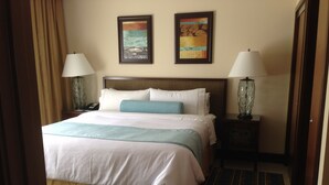 Quarto de hotel com uma cama grande, duas mesas de cabeceira com luminárias, uma cabeceira e dois quadros pendurados na parede.