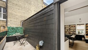 Un intérieur moderne avec un mur en bois foncé, un coin salon avec un banc et des fauteuils, et un espace cuisine comprenant une table à manger et des étagères.