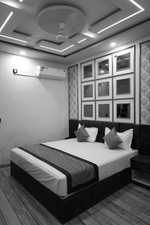 A modern bedroom with a large bed, a ceiling fan, recessed lighting, and a wall-mounted air conditioner. - Hotel The Grand Bareilly (Bareilly)