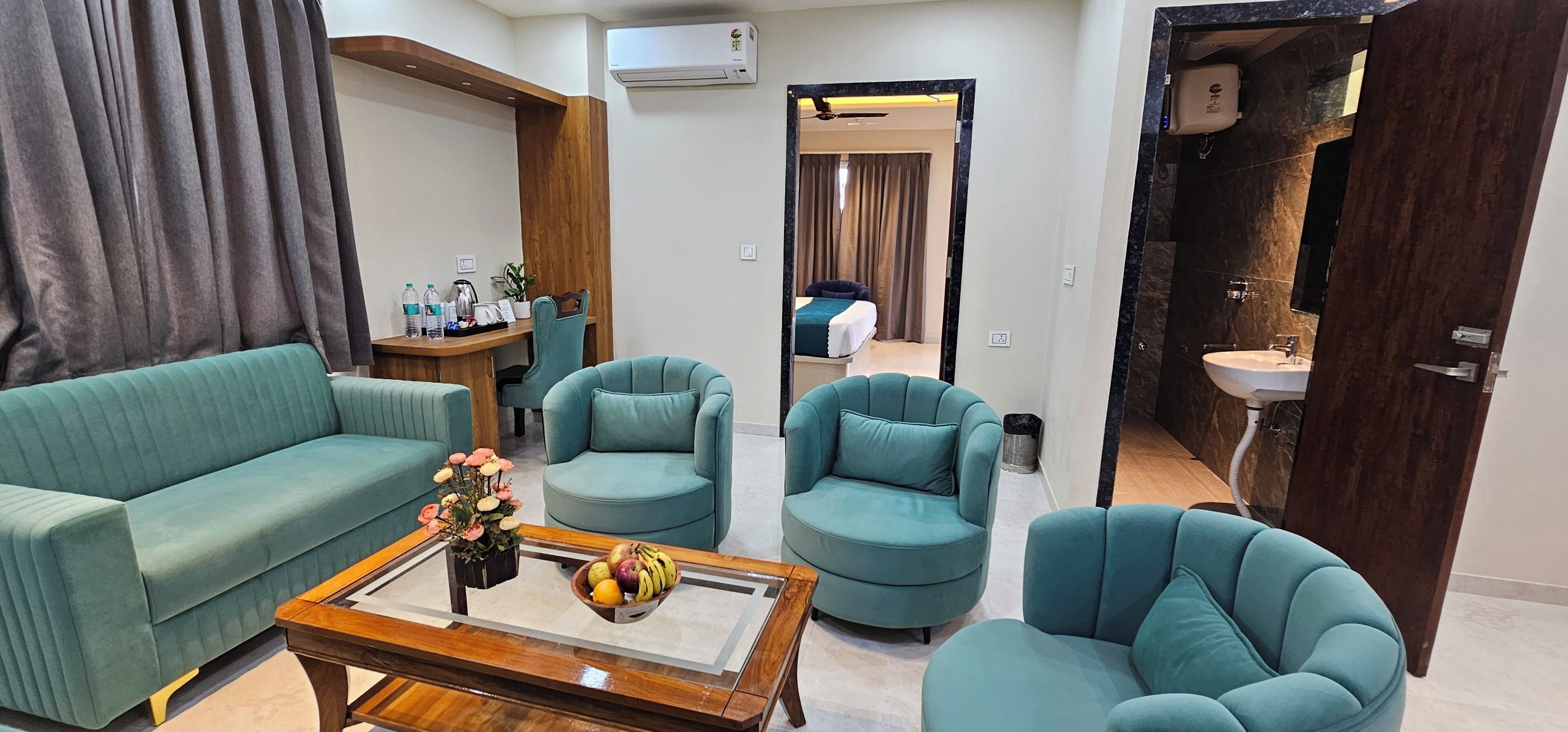 Uma sala de estar moderna com um sofá, duas poltronas, uma mesa de centro com frutas e vista para um quarto.