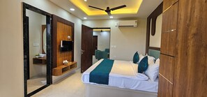 A hotel room with a bed, a TV, a wardrobe, a mirror, and a ceiling fan. - The Sky Comfort Braj dham (Nathdwara)