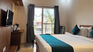 Et hotelværelse med seng, skrivebord, ventilator og et vindue med gardiner.