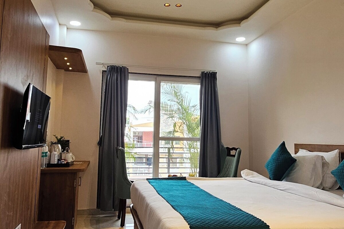 A hotel room with a bed, a desk, a ceiling fan, and a window with curtains.