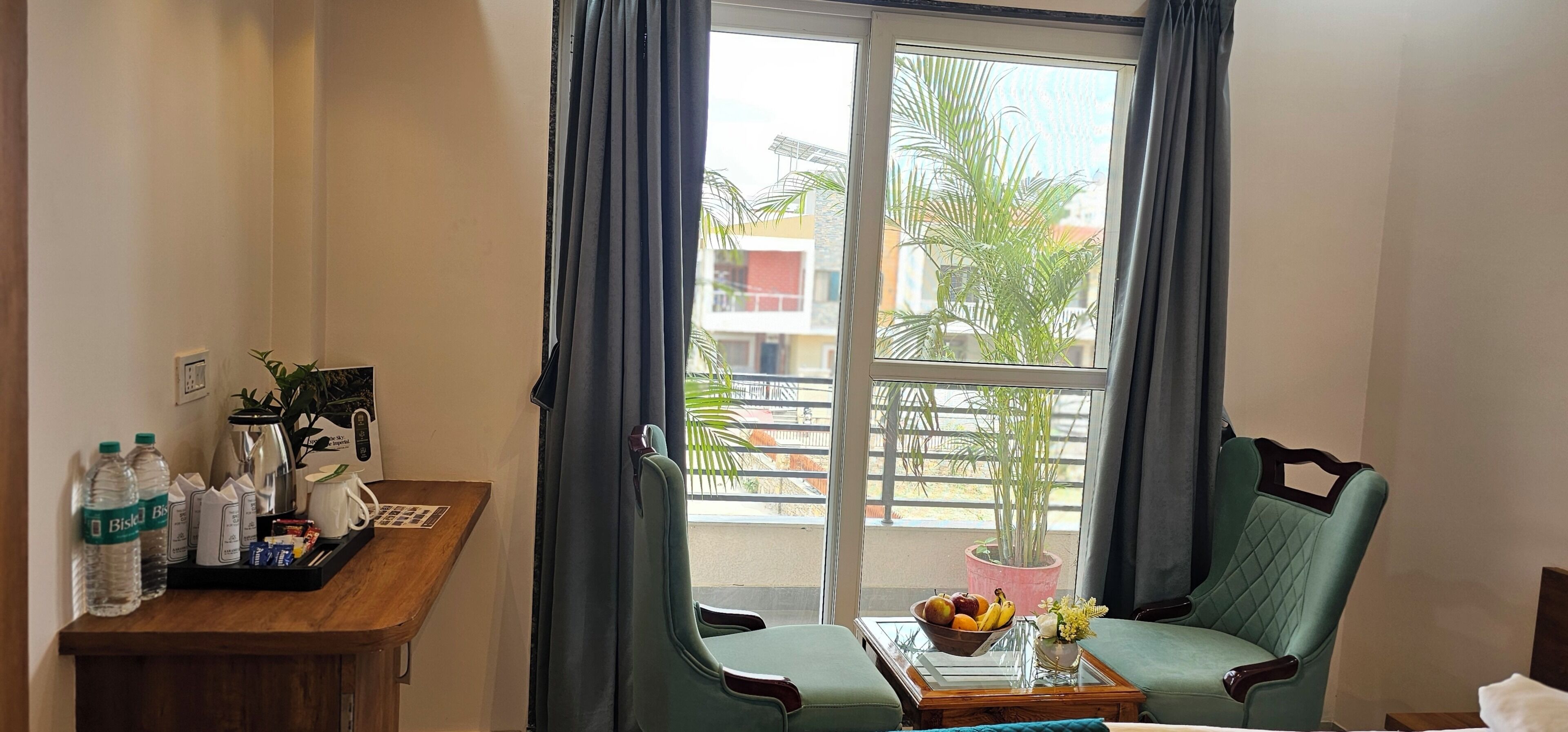 Una habitación con un escritorio de madera, una silla, una mesa con un frutero y un ventanal con cortinas.