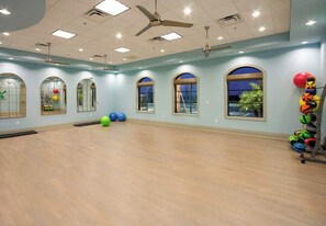 Une pièce spacieuse dotée de grandes fenêtres, d’un ventilateur de plafond et de ballons d’exercice.