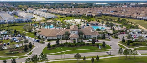 A residential area with a large house featuring a swimming pool, surrounded by parked cars and lush greenery.