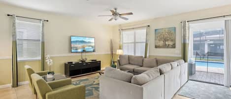 A living room with a gray sectional sofa, a green armchair, a TV, and a painting on the wall.
