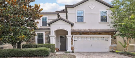 A two-story house with a garage, stone facade, and a well-maintained front yard.