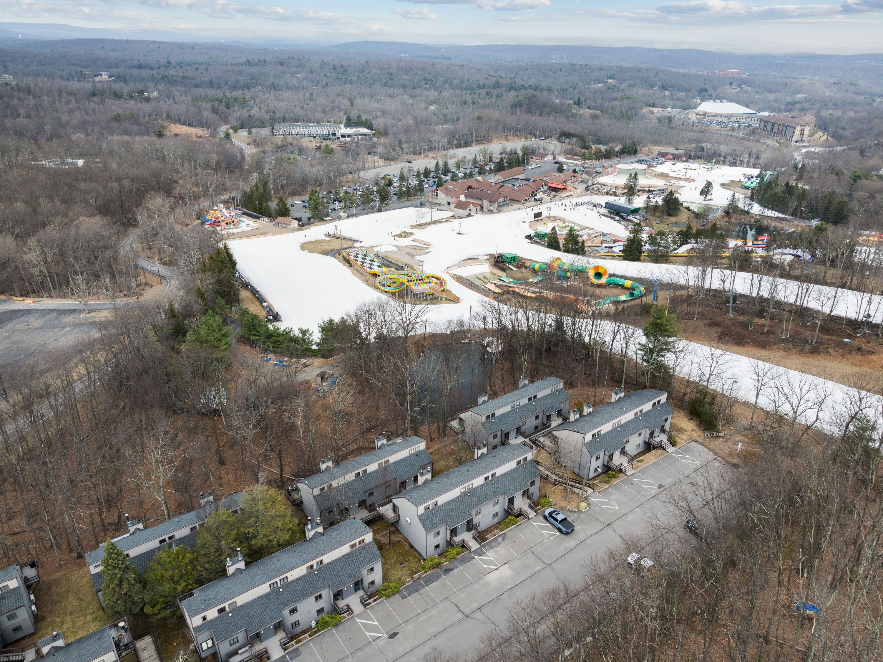 An aerial view of a residential area with multiple buildings, a parking lot, and a playground.