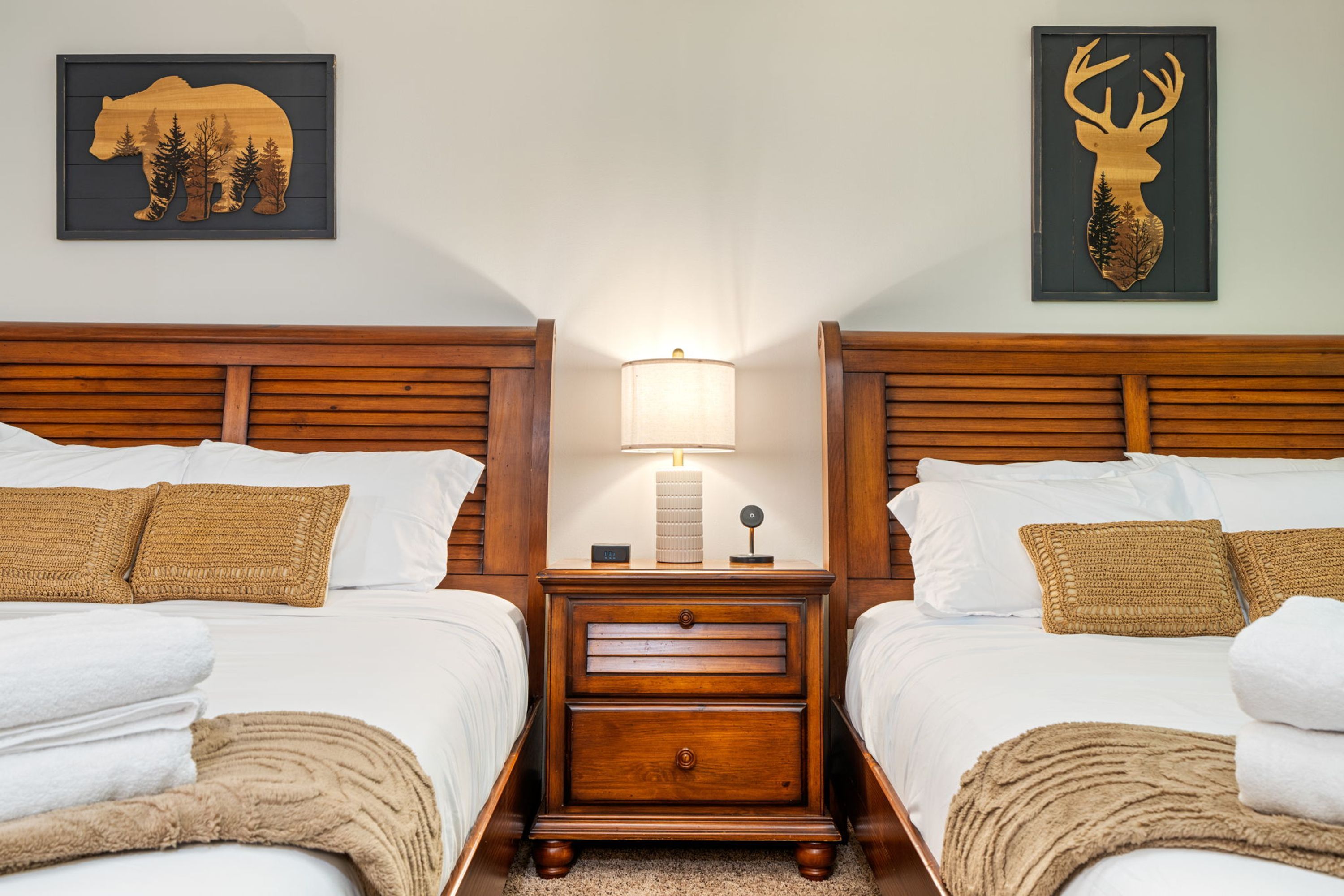 A hotel room with two wooden beds, a nightstand with a lamp, and two wall-mounted animal-themed decorations.
