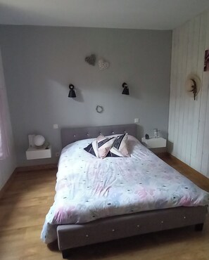 Une chambre à coucher comprenant un lit, des tables de chevet, des lampes fixées au mur et une petite étagère ornée d’objets décoratifs.
