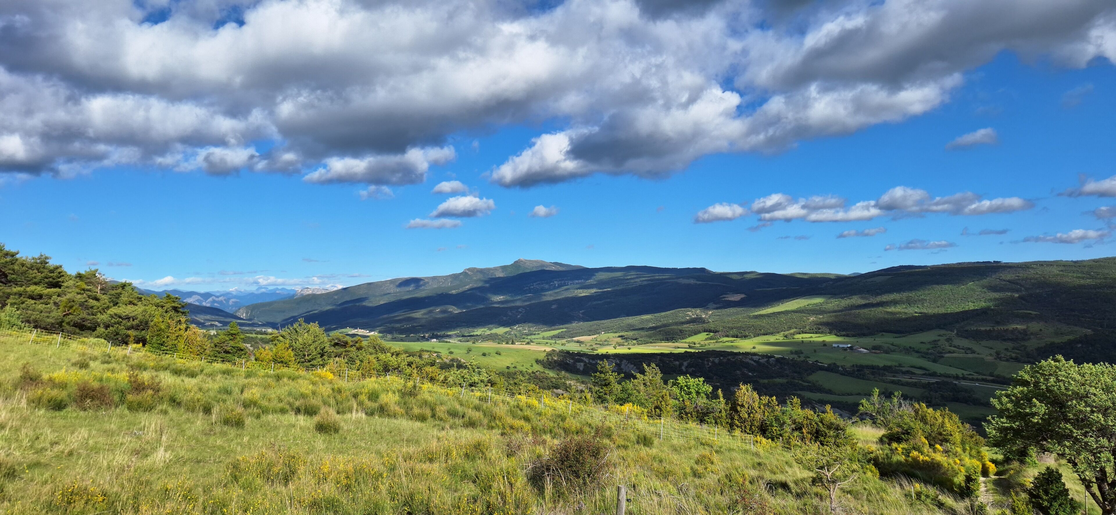 Paisaje montañoso con cielo despejado y una zona vallada al frente.