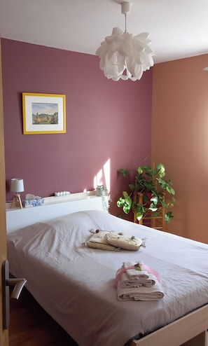 Une chambre à coucher avec un lit, une table de chevet, une lampe, un tableau encadré au mur et une plante en pot.