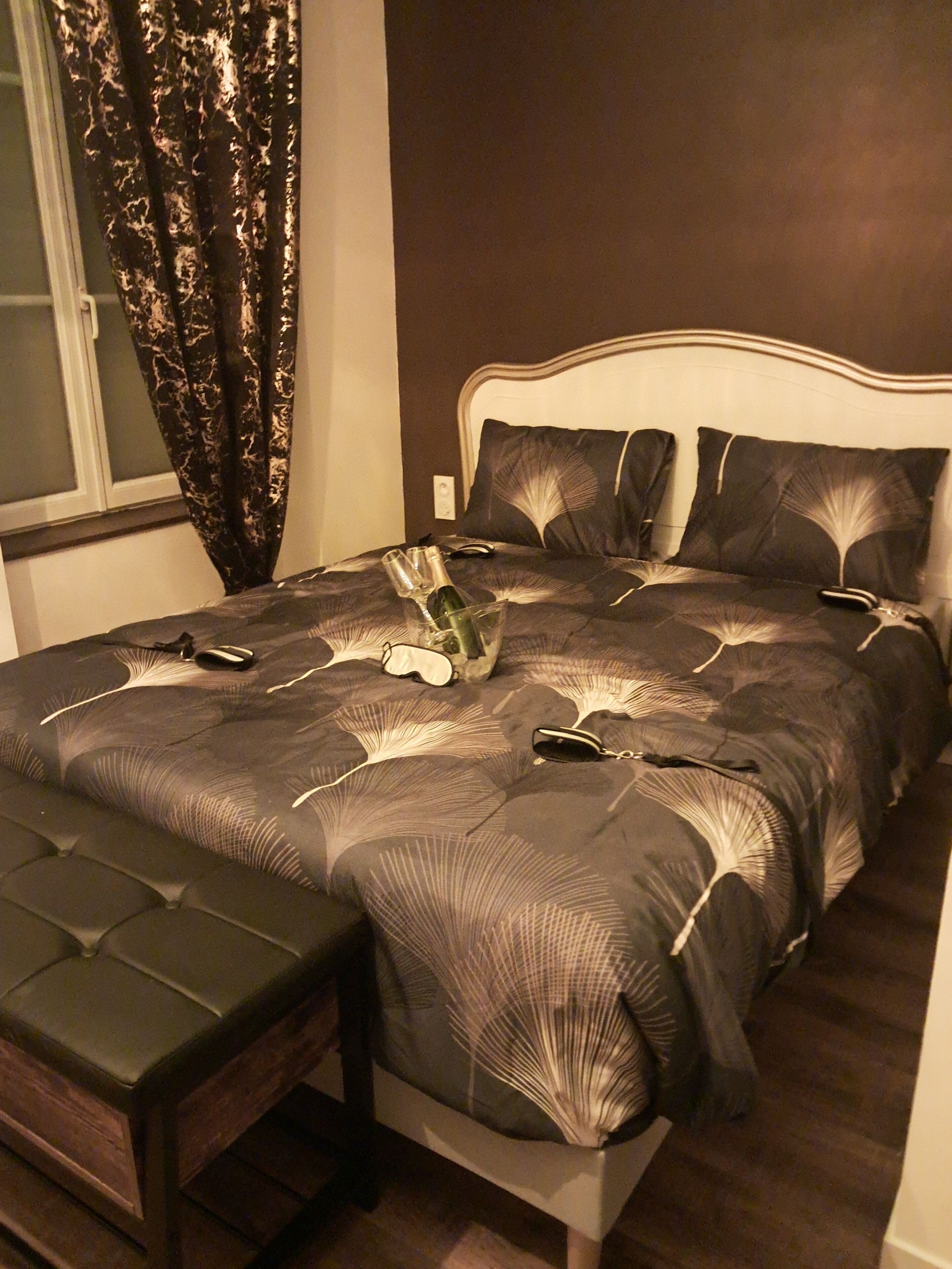 Een slaapkamer met een bed, een bankje en een raam met gordijnen.