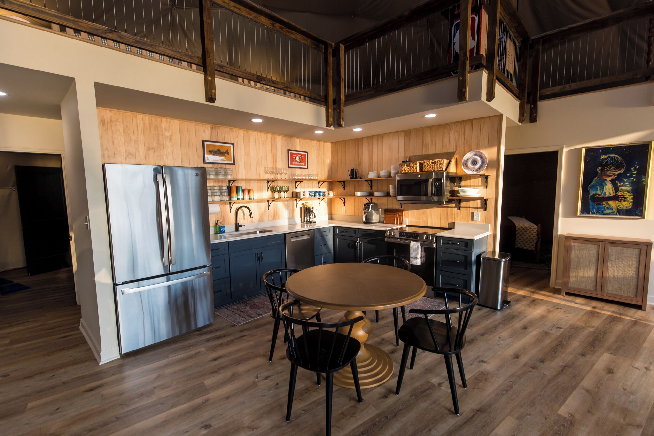 A modern kitchen with a stainless steel refrigerator, wooden cabinets, and a dining area with a round table and chairs.