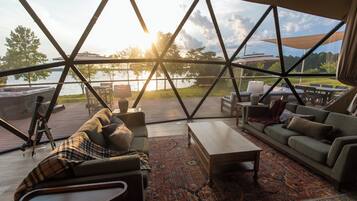 A modern interior with a large glass window overlooking a lake, furnished with a sofa, coffee table, and chairs.
