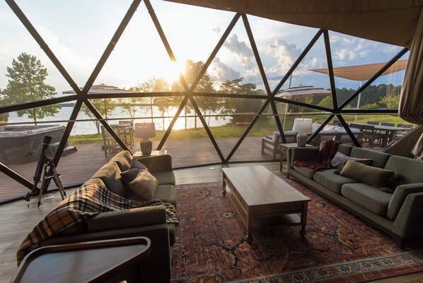 A modern interior with a large glass window overlooking a lake, furnished with a sofa, coffee table, and chairs.