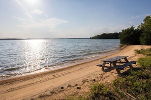 A sandy beach with a wooden picnic table and a clear view of a lake. - Lake Monticello Geodome-MiniGolf-Hot Tub-Games-Playground-Stargazing-Lake Murray (Jenkinsville)