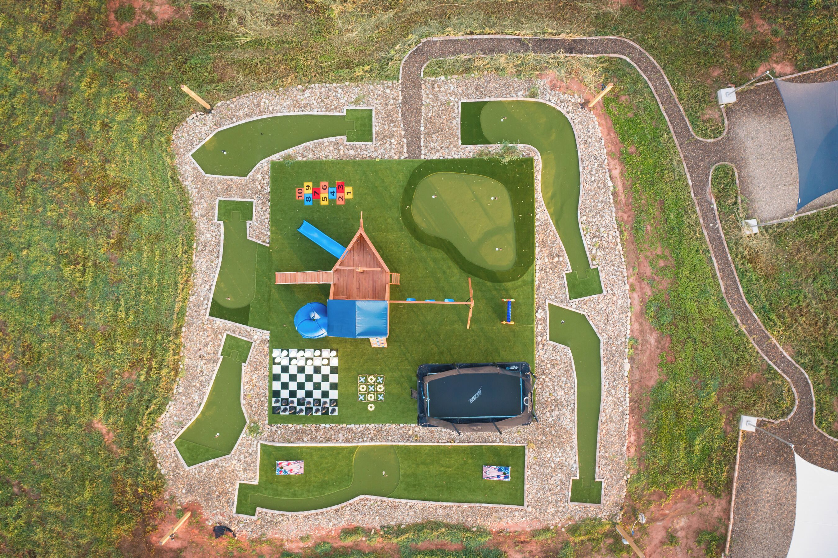 A fenced outdoor area with a playground, a small building, a pool, and a checkered game board.